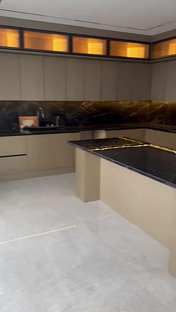 Sand-lacquered kitchen with black marble worktops and a backlit glass display column